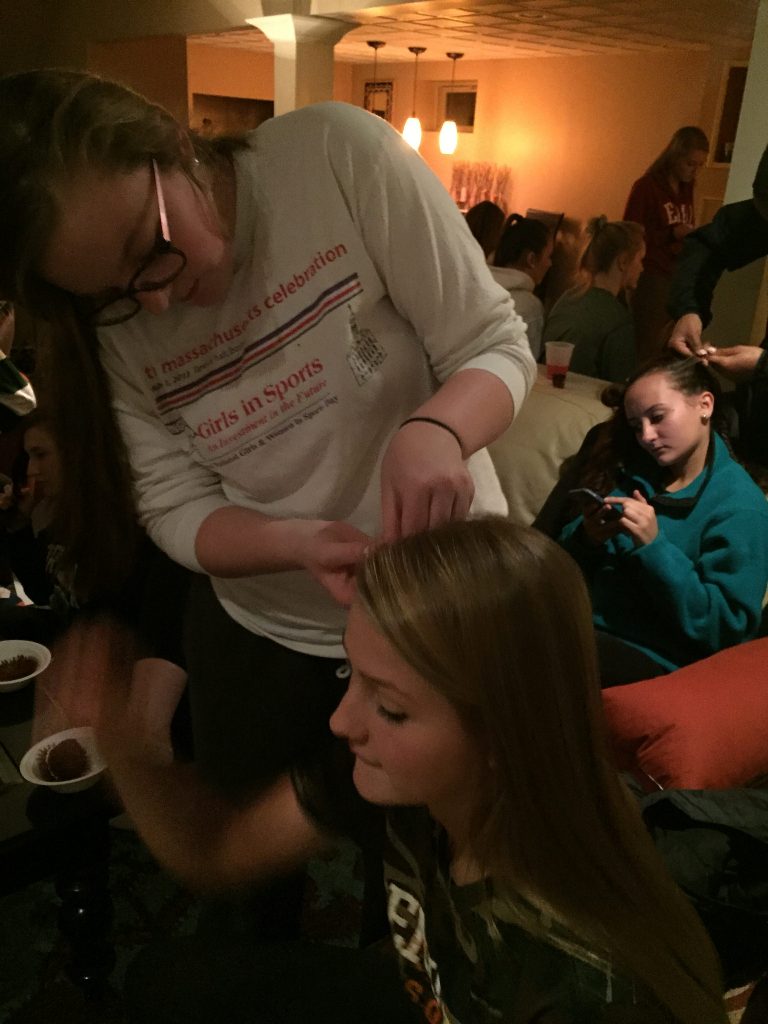 The night before the big game, senior Brigid Marquedant (standing) cornrows the hair of the senior girls, starting with Emily Hoffman (sitting). Photo by Emma Zack.