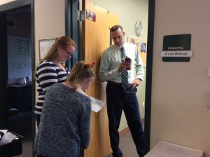 Hannah Murphy (left) and Riley Meyers read the Daily Grind script as they deliver coffee to Principal Evan Bishop. Photo by Julia Joshi.